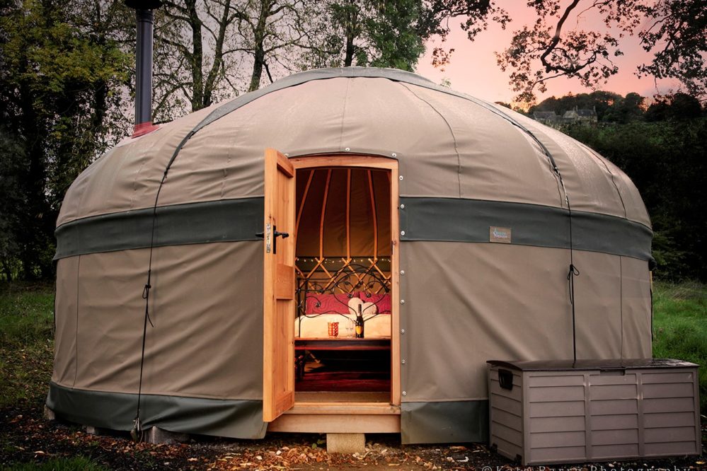 Yurt at sunset with door open and bed and lights visible