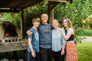 About Us - Glamping site host family standing next to lit pizza oven